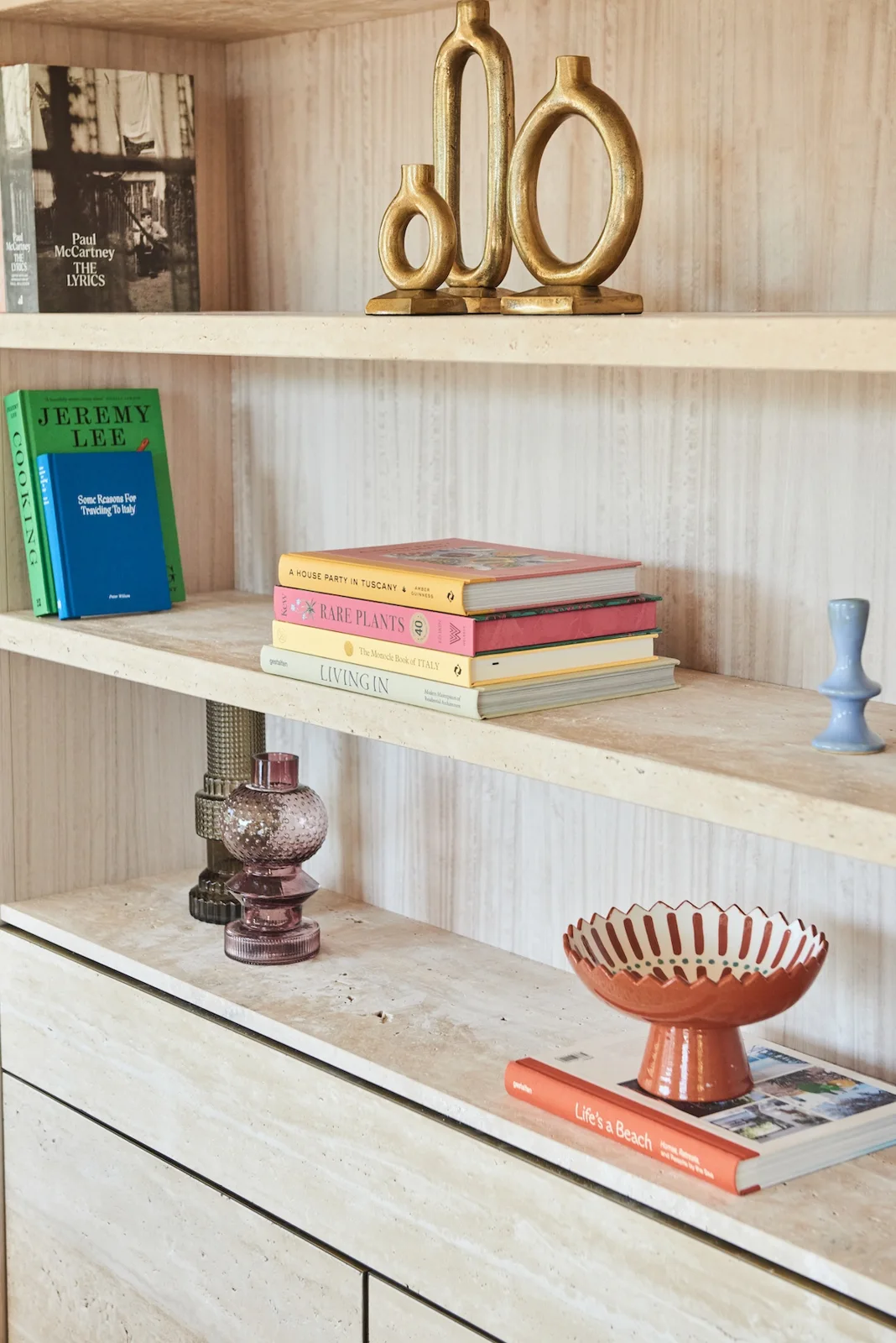 Pale timber shelving with books, objects and sculptural brass accessories